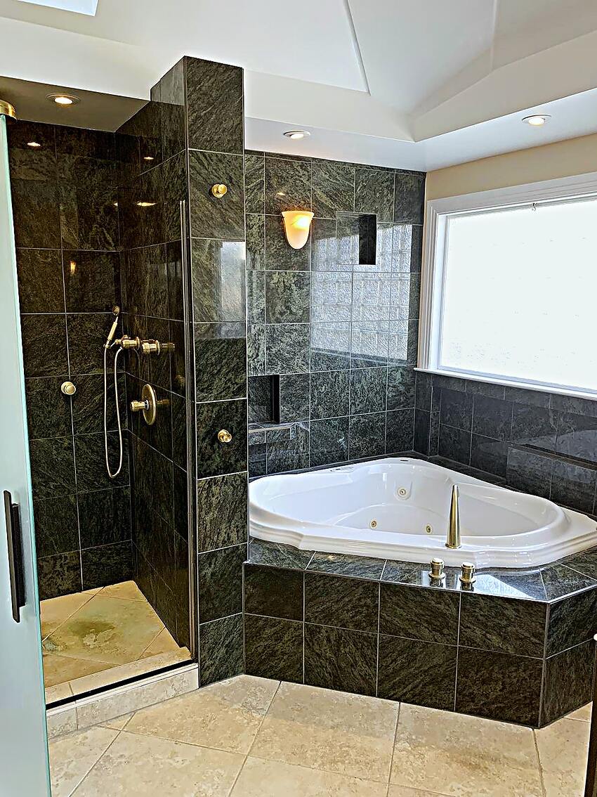 Green marble bathroom with corner tub and glass shower